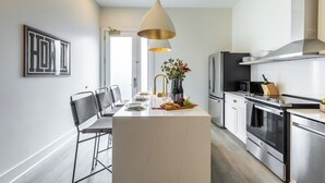 Et moderne køkken med en central ø, rustfrie stålapparater og en hængende lampe.