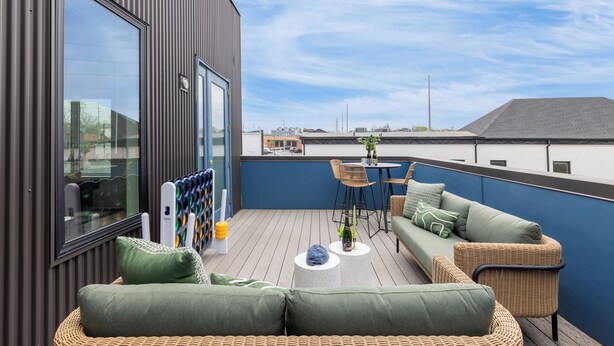 En tagterrasse med moderne design, med et siddeområde bestående af en sofa, stole, et lille bord og et stort vindue.
