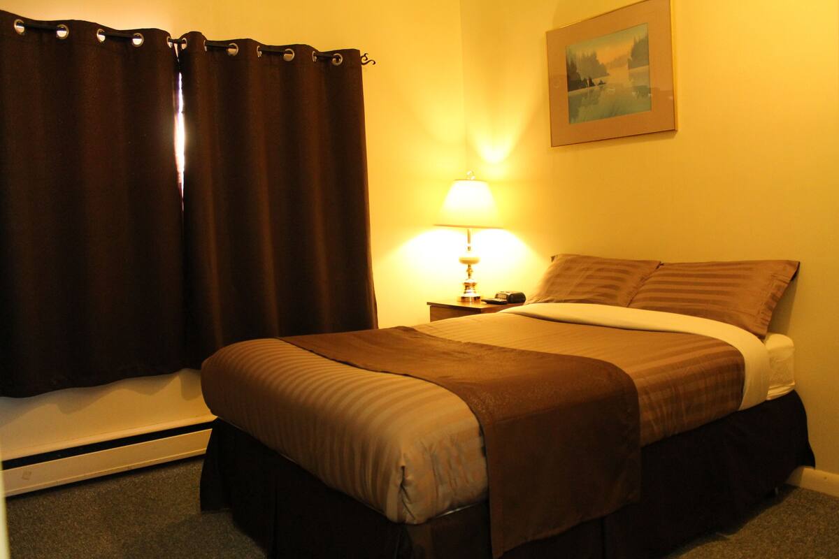 Una habitación de hotel con cama, mesita de noche, lámpara y un cuadro en la pared.