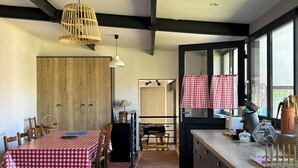 A kitchen with a dining area, wooden wall, and checkered curtains. - UNE Maison DE Famille A LA Campagne (Gièvres)