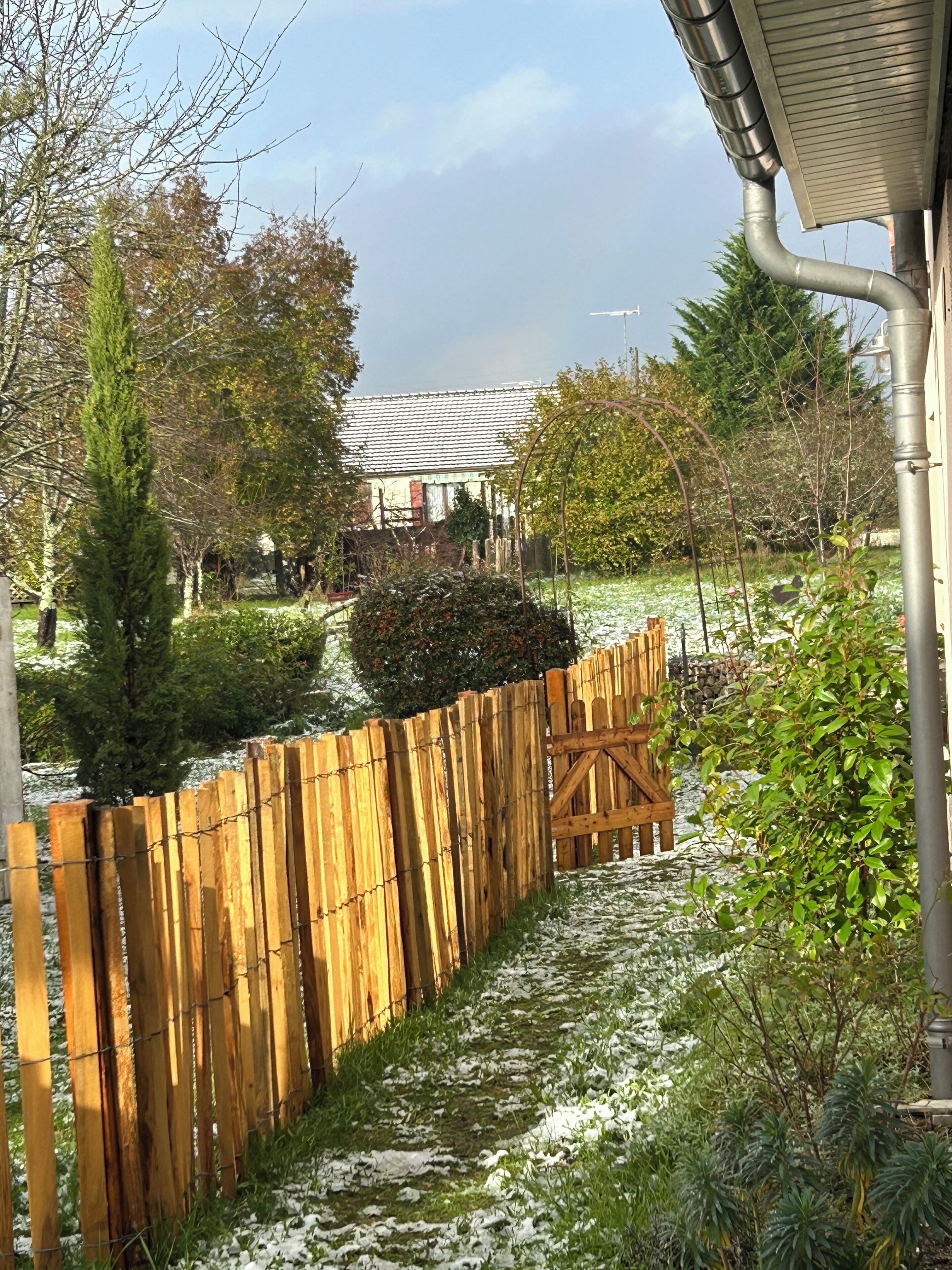 A wooden fence, a gate, and a pathway leading to a house with a tiled roof.