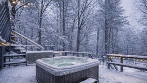 Ein hölzerner Whirlpool, umgeben von schneebedeckten Bäumen, mit einer Holzterrasse und Geländer.