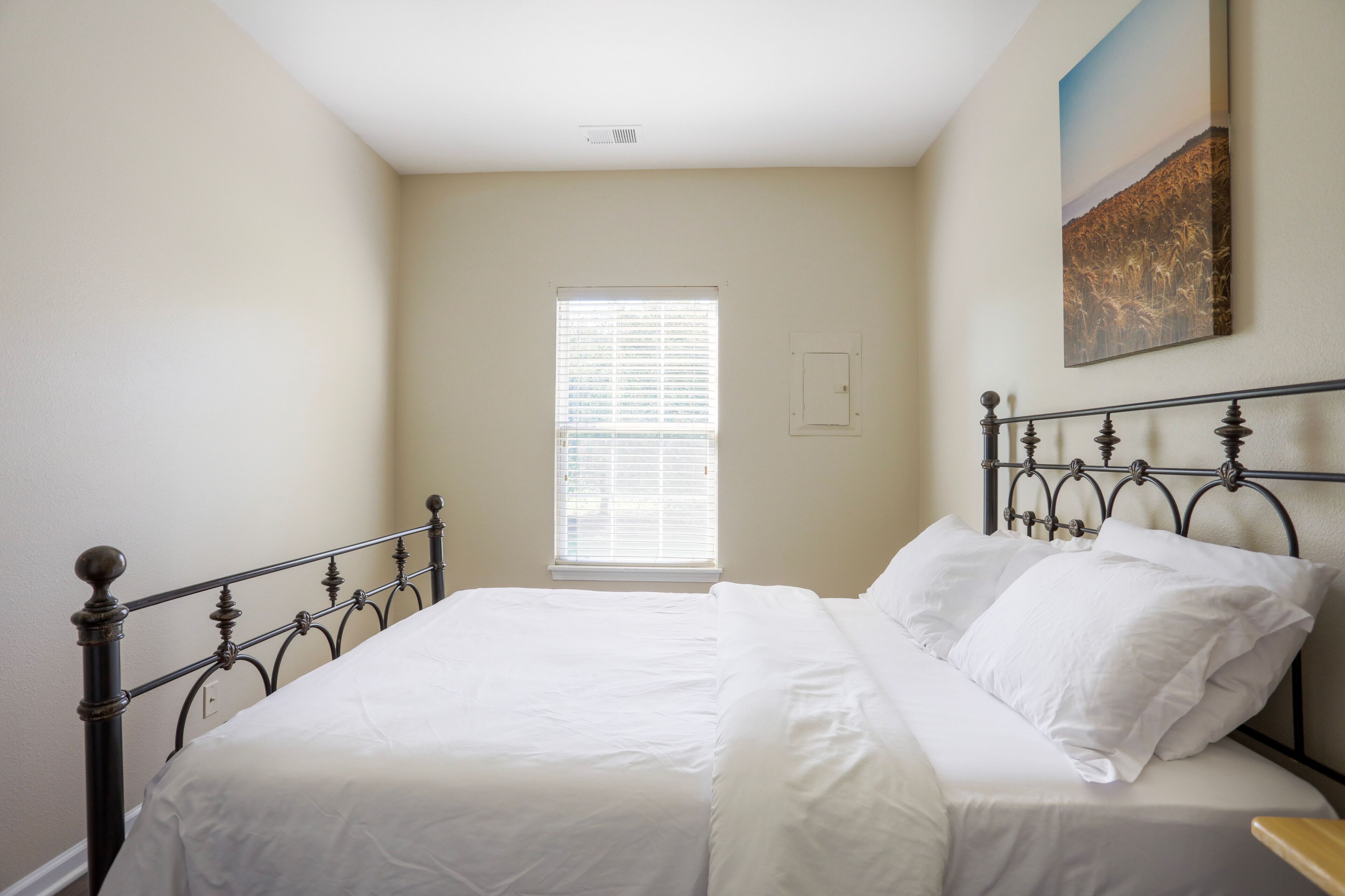 A bedroom with a single bed, a window with blinds, and a painting on the wall.