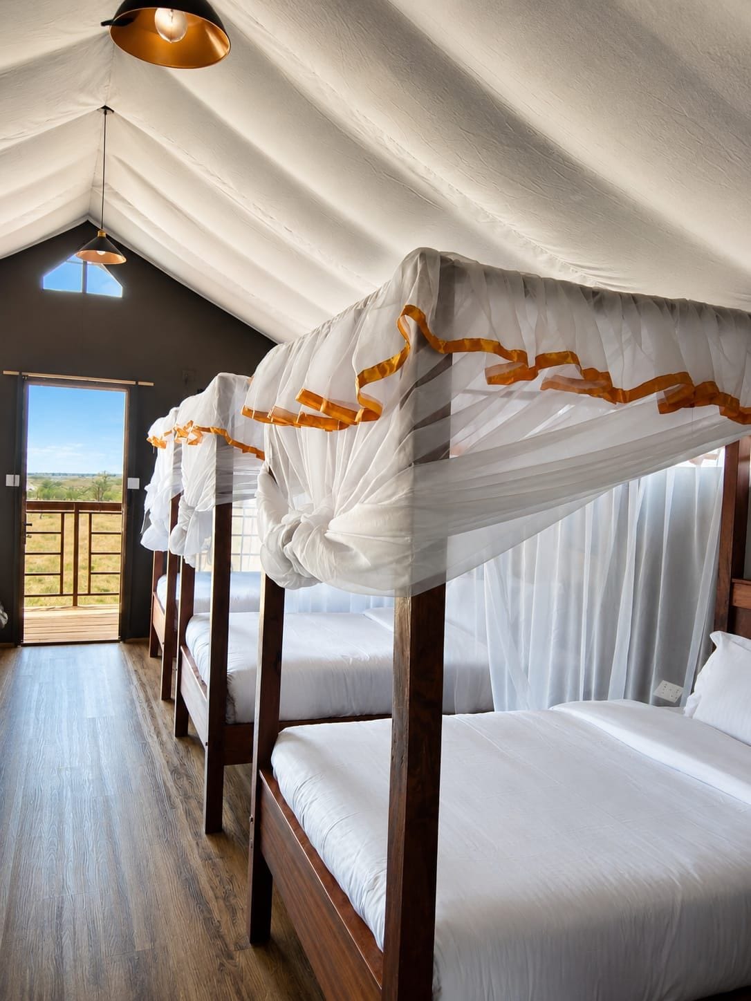 A hotel room with a wooden bed frame, white bedding, and a view through a large window.