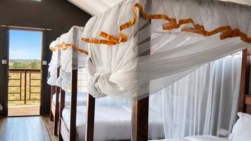 A hotel room with a wooden bed frame, white bedding, and a view through a large window.
