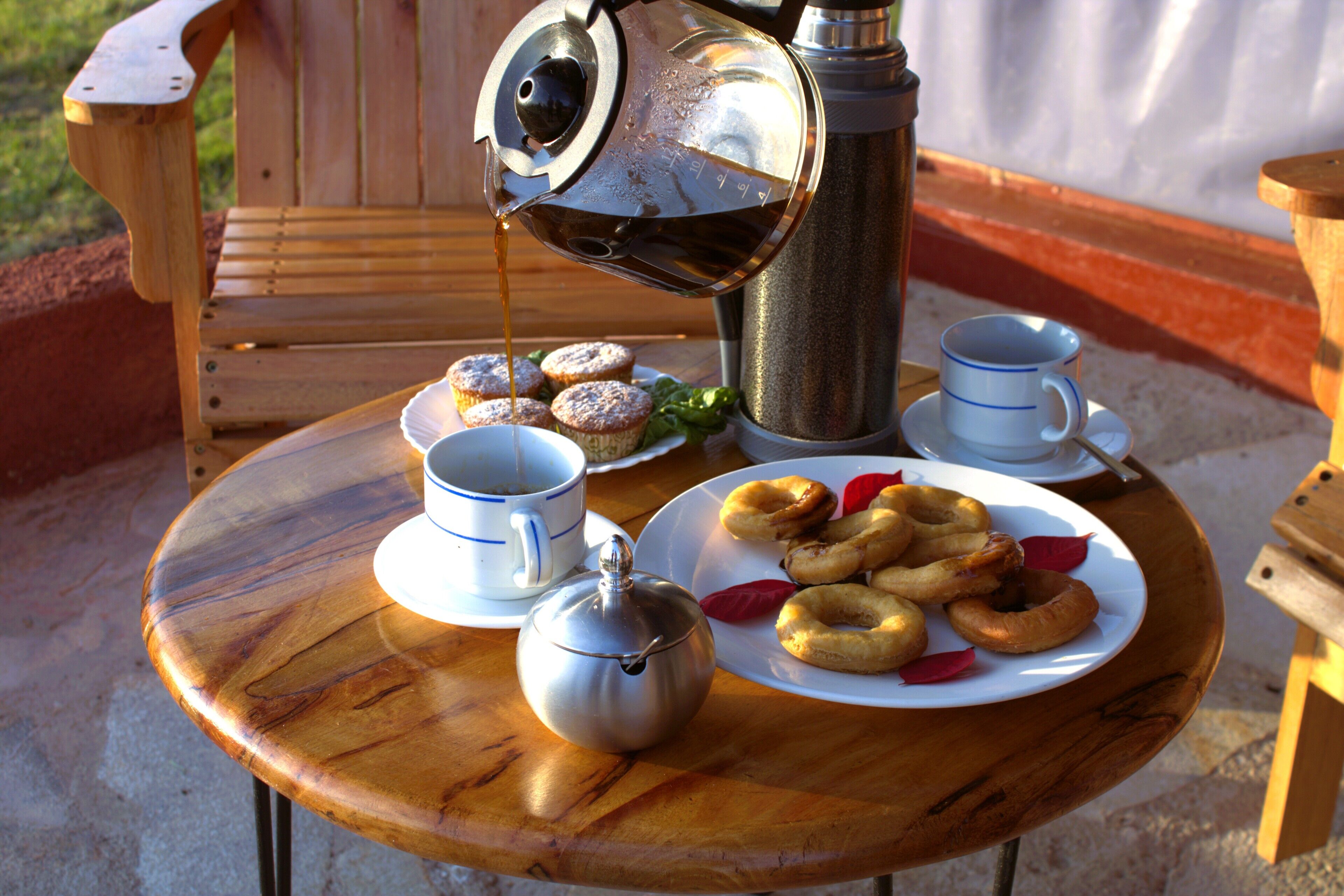 A wooden table with a metal teapot, a cup, and a plate with pastries.