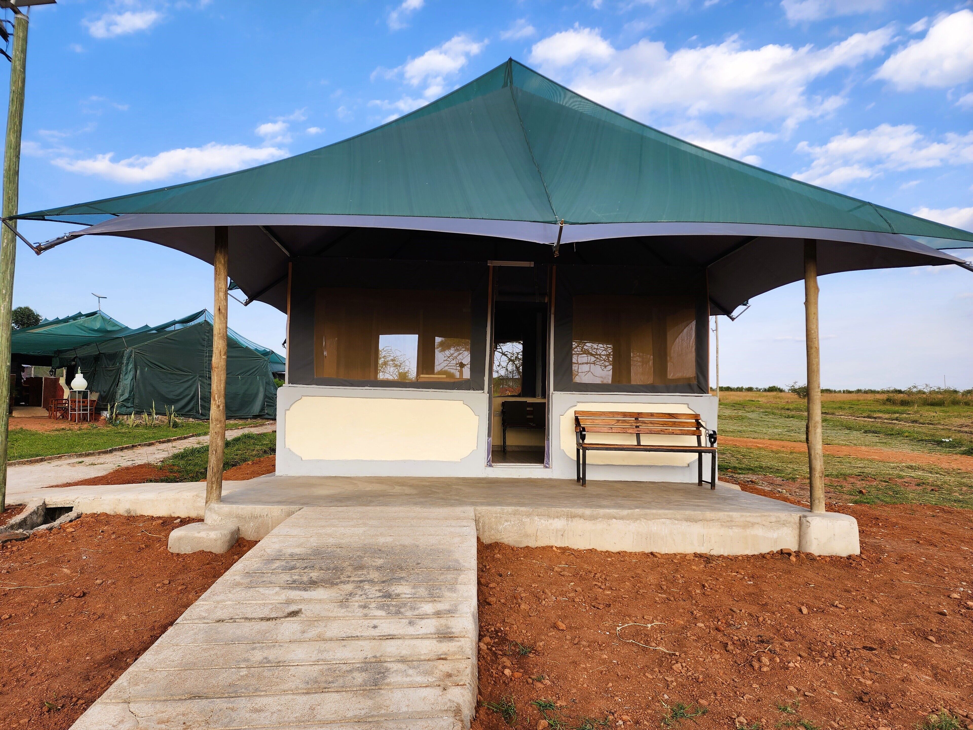 A covered pavilion with a bench, a concrete pathway leading to it, and a dirt path beside it.