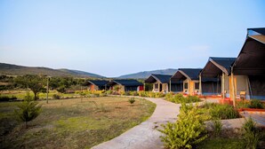 A row of modern, single-story tents with a pathway leading to them, set in a grassy area with hills in the background. - Endeem Mara Resort (Maasai Mara)