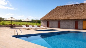 A swimming pool with lounge chairs and a thatched-roof building. - Endeem Mara Resort (Maasai Mara)