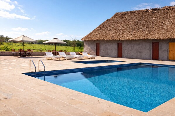 A swimming pool with lounge chairs and a thatched-roof building. - Endeem Mara Resort (Maasai Mara)