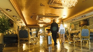 A luxurious lobby with ornate golden decor, a grand chandelier, and a reflective marble floor.
