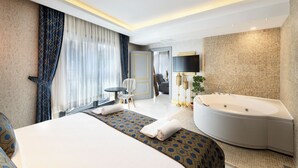 A modern hotel room with a large bed, a separate seating area, a large bathtub, and a flat-screen TV.