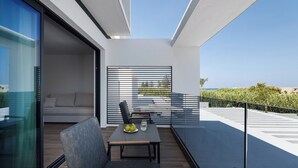 A modern balcony with a glass door leading to a living area, a table with a vase and fruit, and a view of the landscape. - Nuera II: Modern 4BR Villa, 300m from the Beach (Chania)