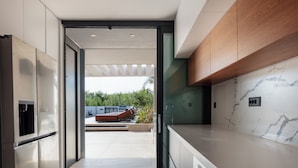 A modern kitchen with built-in appliances, a marble backsplash, and a view of an outdoor patio area. - Nuera II: Modern 4BR Villa, 300m from the Beach (Chania)