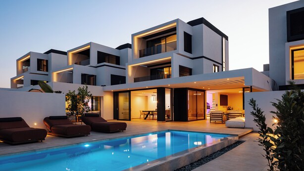A modern house with a swimming pool, outdoor seating, and a well-lit interior.
