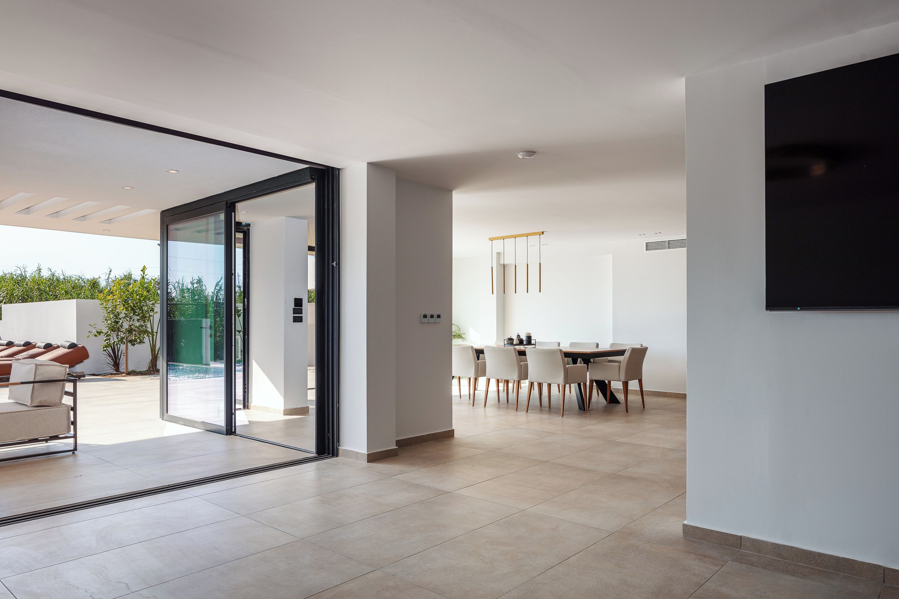 A modern interior with a dining area, a large glass door leading to an outdoor space, and a flat-screen TV mounted on the wall.