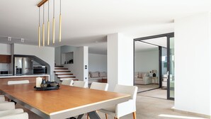 A modern kitchen with stainless steel appliances, a wooden dining table with white chairs, and a staircase leading to a living area.