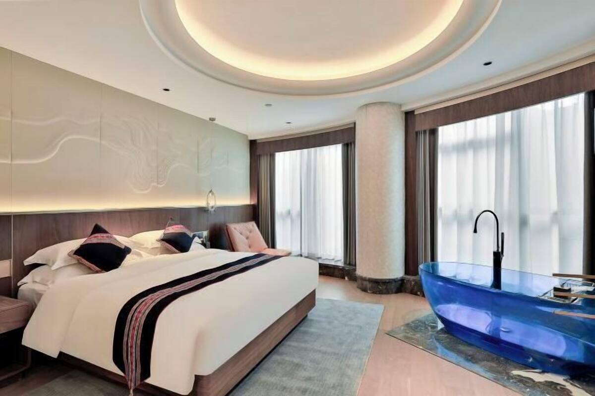 Une chambre d’hôtel moderne avec un grand lit, une baignoire en verre et une vue sur la ville.
