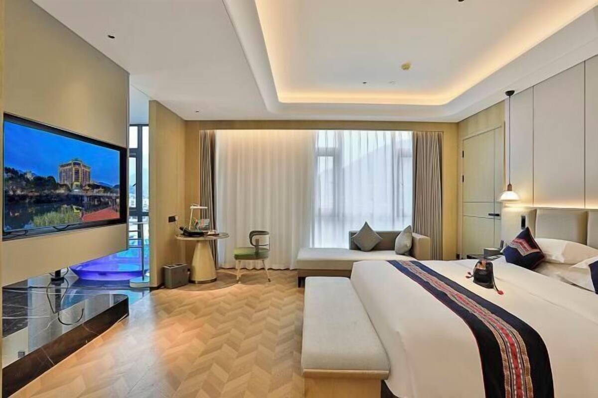 Une chambre d’hôtel avec un grand lit, une télévision, un bureau avec une chaise et une fenêtre avec des rideaux.