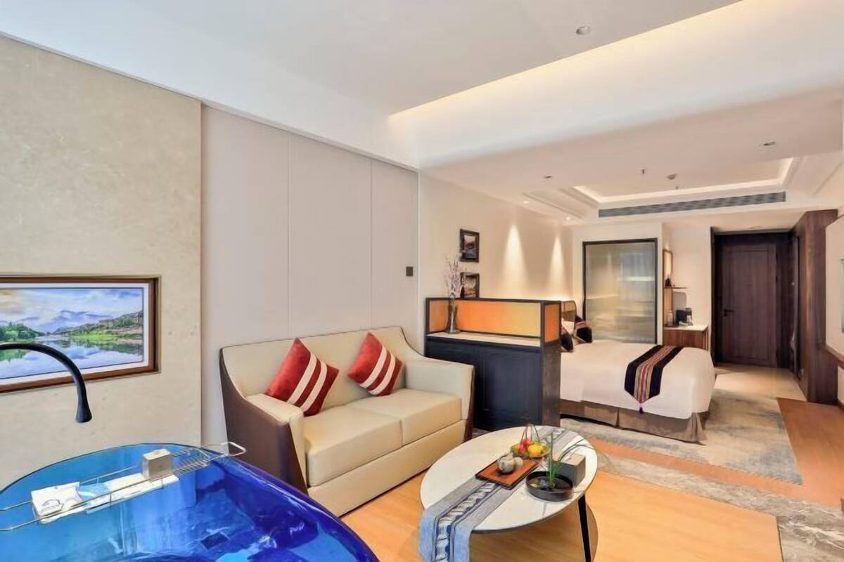 Une chambre d’hôtel avec un canapé, un lit, un bureau, une chaise, une table basse et une grande baignoire bleue.