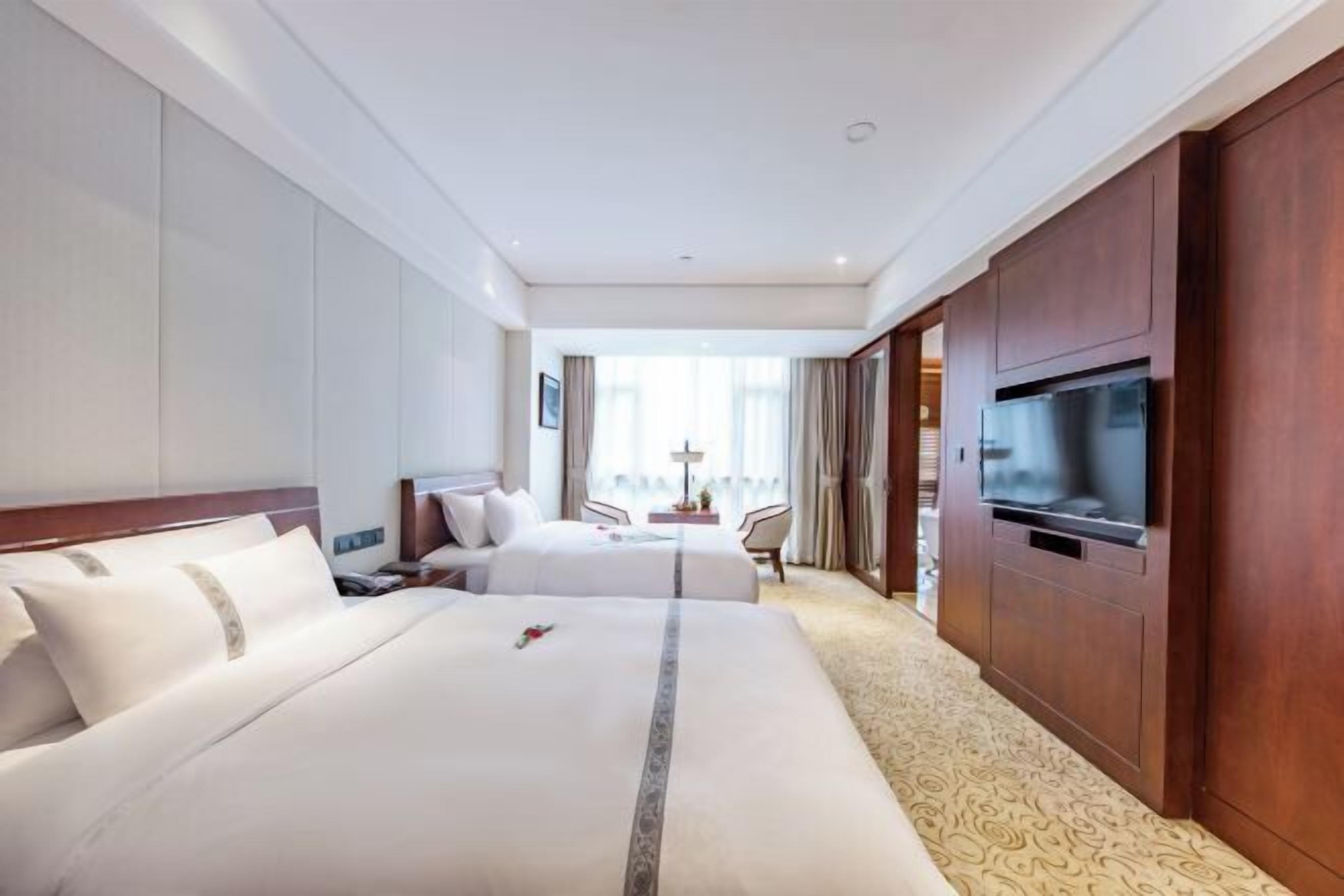 A hotel room with two beds, a TV, and a view of the outdoors.