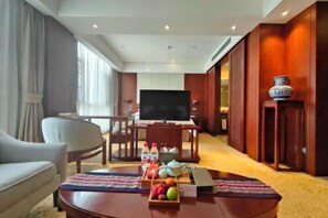 A hotel room with a sofa, a coffee table with fruit and drinks, a TV, and a wooden cabinet. - Shexiang Hongbin Hotel (Jingning)