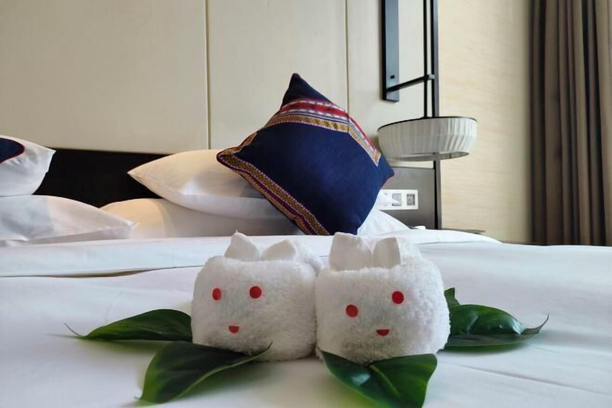 A neatly made bed with white bedding, a blue pillow with a colorful border, and two white plush toys resembling animals.