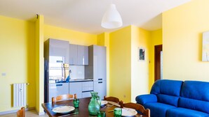 A dining area with a wooden table set for four, a blue sofa, and a kitchen in the background. - Sunny Home by Interhome (Santo Stefano al Mare)