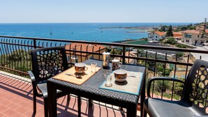 A balcony with a table set for two, overlooking a coastal view with buildings and the sea. - Sunny Home by Interhome (Santo Stefano al Mare)