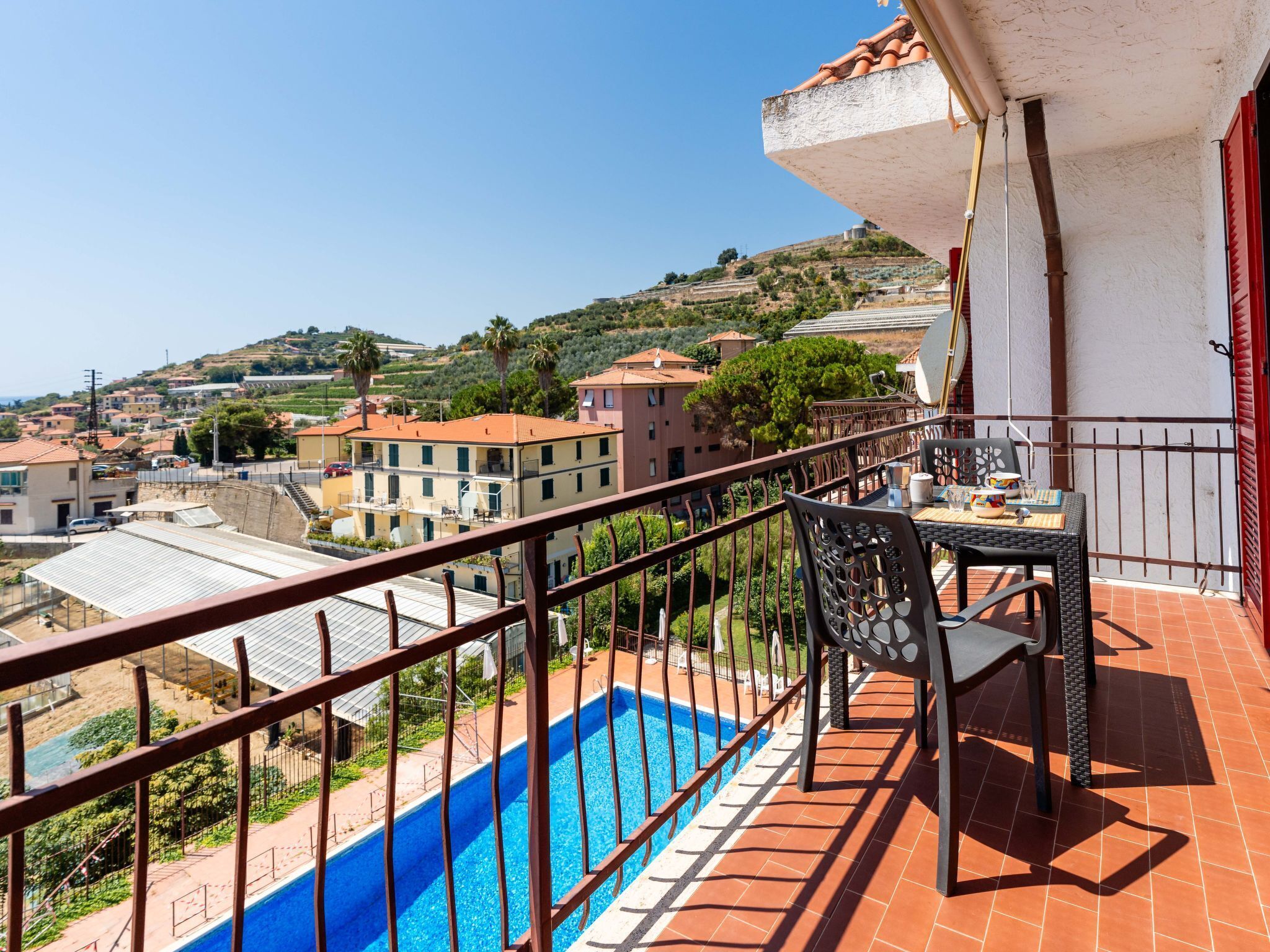 Uma varanda com piscina, com vista para uma área residencial com casas escalonadas e uma encosta.