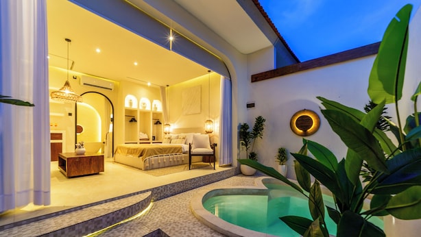 A modern interior with a pool, a living area with a sofa and a dining table, and a kitchen visible through an open doorway. - OriVista Luxe 1BR Designer Pool Villa in Canggu (Canggu)