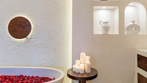 A spa-like setting with a large white bathtub filled with red rose petals, a wooden circular window, and a small table with white candles. - OriVista Luxe 1BR Designer Pool Villa in Canggu (Canggu)