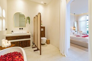A modern bathroom with a bathtub filled with rose petals, a large mirror, and a wooden vanity. - OriVista Luxe 1BR Designer Pool Villa in Canggu (Canggu)