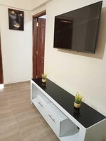 A modern living room with a black TV stand, a flat-screen TV, and two small potted plants.