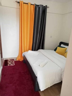 Un dormitorio con una cama, una alfombra roja y una cortina.