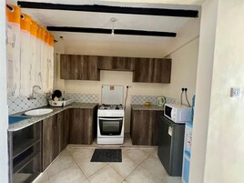 A compact kitchen with dark wooden cabinets, a white stove, a sink, and a microwave.