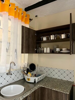 Una cocina con encimera de granito, un lavabo blanco y un escurreplatos. Hay armarios sobre la encimera y una ventana con cortinas.