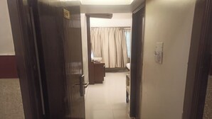 A hotel hallway with a door leading to a room, a small desk with a chair, and a bed with curtains. - Golden Residency (Bengaluru)