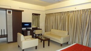 A hotel room with a bed, a sofa, a chair, a small table, a television, and curtains. - Golden Residency (Bengaluru)