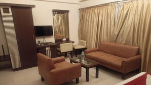 A hotel room with a sofa, armchair, a small table with a bottle, a TV, and a mirror. - Golden Residency (Bengaluru)