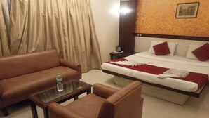 A hotel room with a bed, a brown sofa, a small table, and a nightstand. - Golden Residency (Bengaluru)