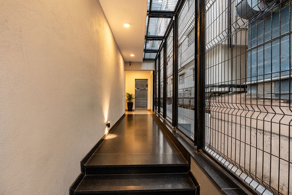 Un pasillo con piso negro, una planta en maceta y una puerta con la etiqueta 'Wandell'.