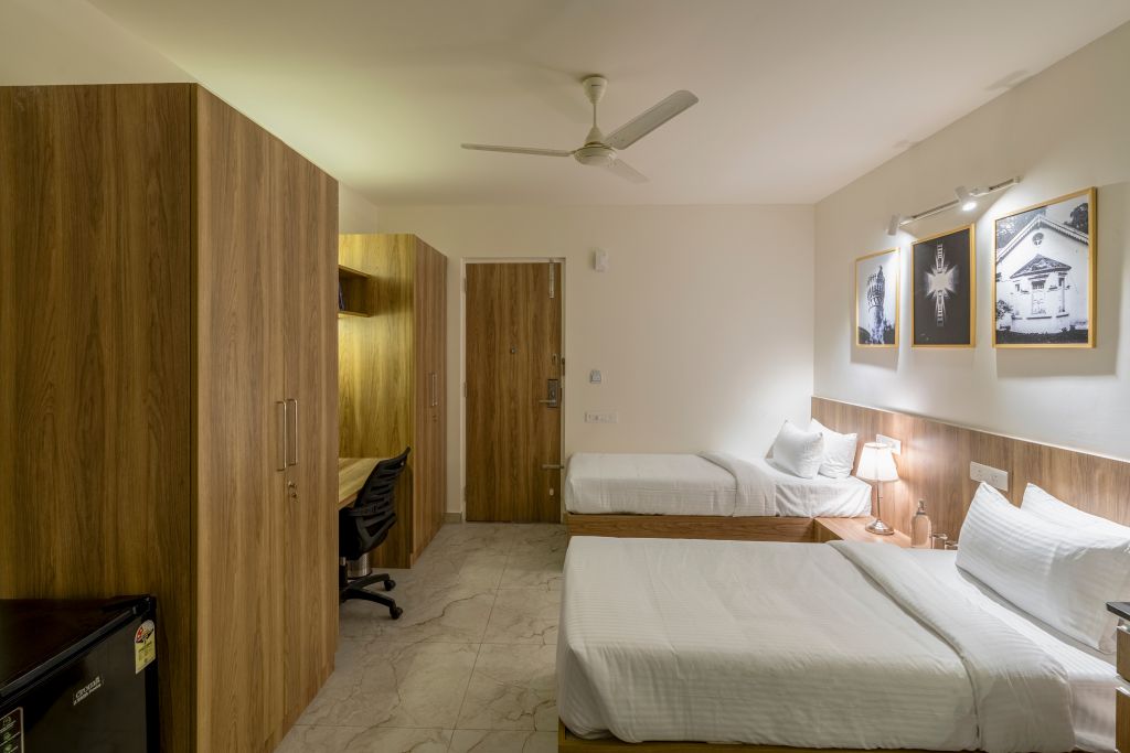 Habitación de hotel con dos camas, un escritorio, una silla, un armario y un ventilador de techo.