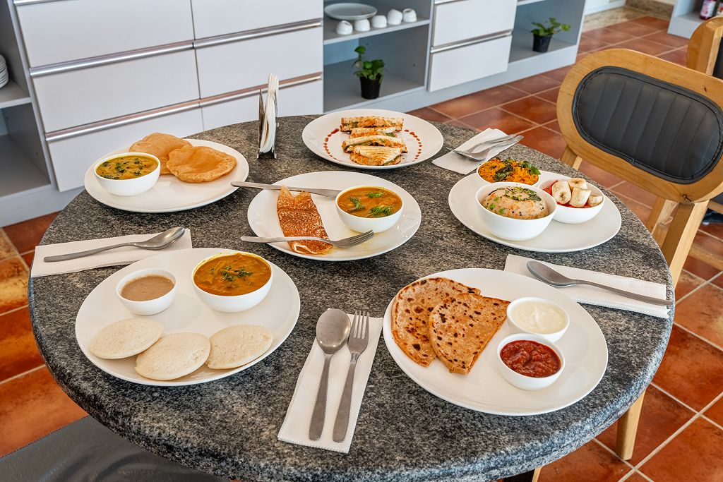 Mesa redonda con diversos platos de comida india, cubiertos y una silla.