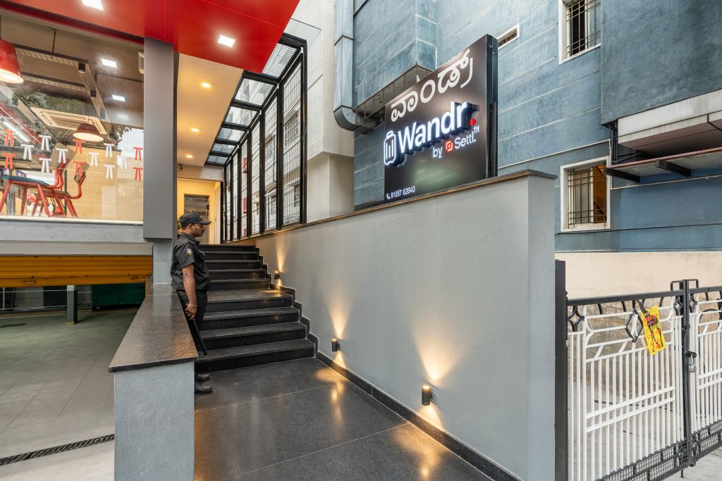 Eine Treppe führt zu einer zweiten Etage, auf der ein Schild mit 'Wandr by Sett'l' und einer Kontaktnummer zu sehen ist.
