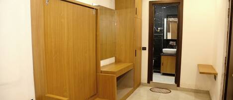 A room with wooden wardrobes, a small bench, and a bathroom with a mirror and sink.