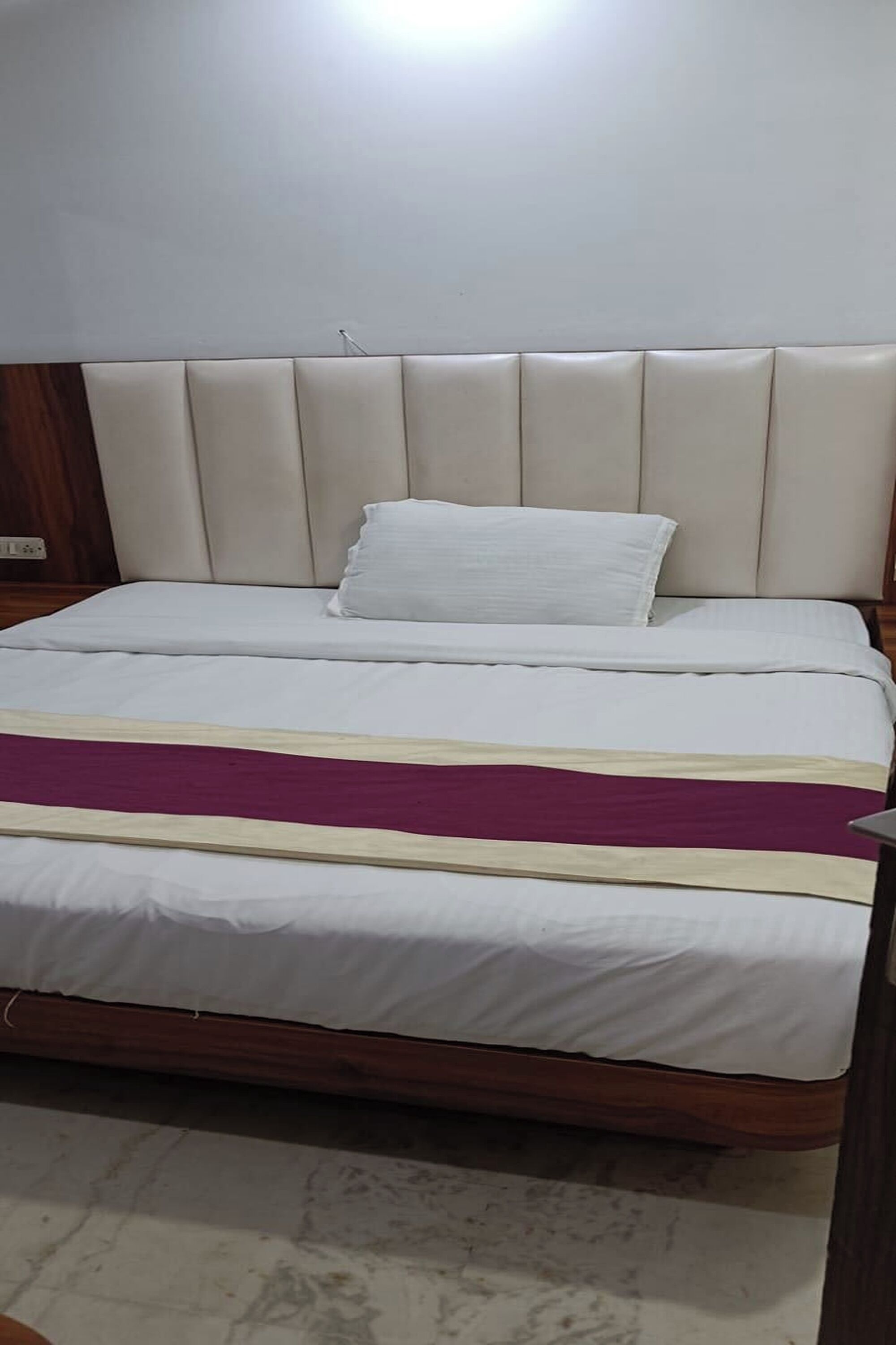 Una cama con cabecera, ropa de cama blanca y una manta morada.