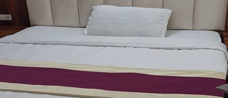 Una cama con cabecera, ropa de cama blanca y una manta morada.