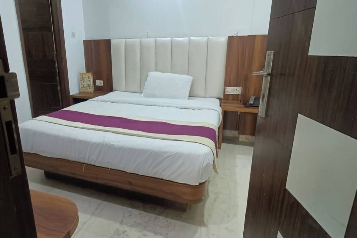 A hotel room with a wooden bed frame, white bedding, a headboard, a bedside table with a lamp, and a nightstand with a phone.