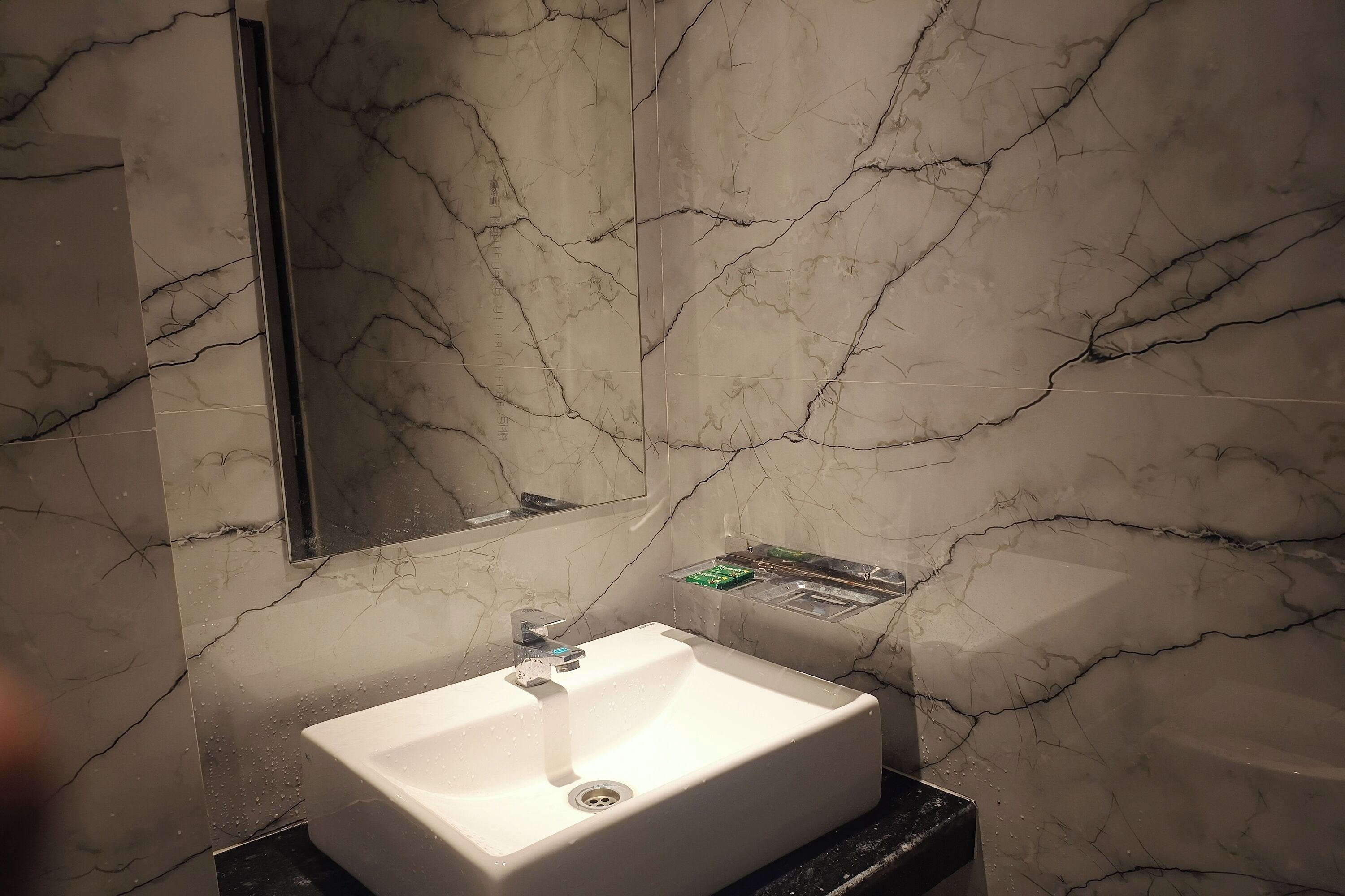 A bathroom with a white sink, a mirror, and marble walls.